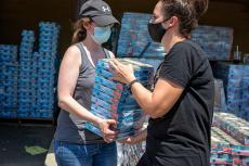 Two masked people moving cases of canned cat food to help an animal shelter