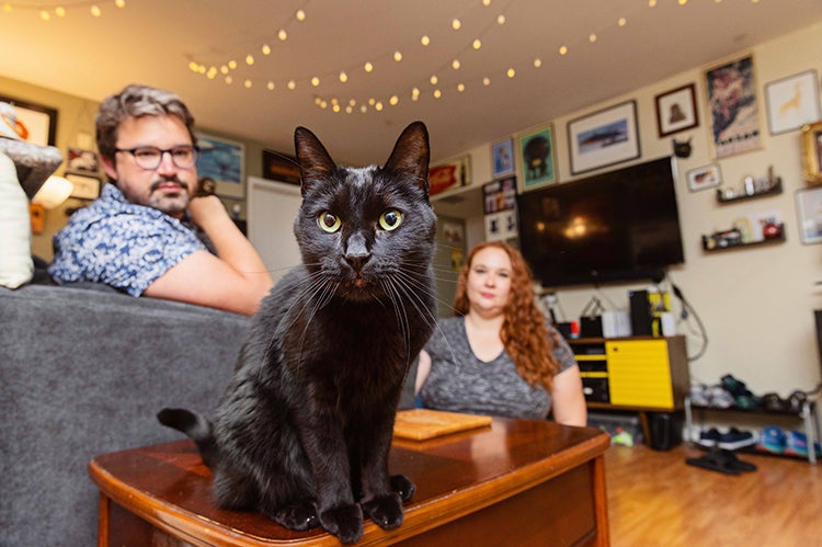 Black cat in the foreground with two people in the background in a home
