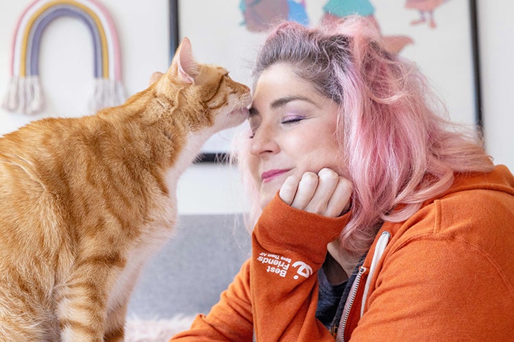 Orange tabby cat licking the forehead of a person wearing a Best Friends sweatshirt