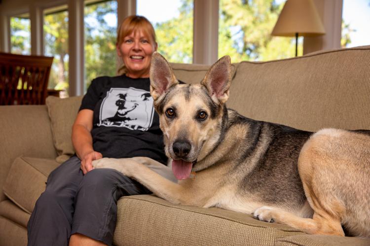 Woman sitting on a couch next to a happy looking German shepherd dog