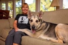 Woman sitting on a couch next to a happy looking German shepherd dog